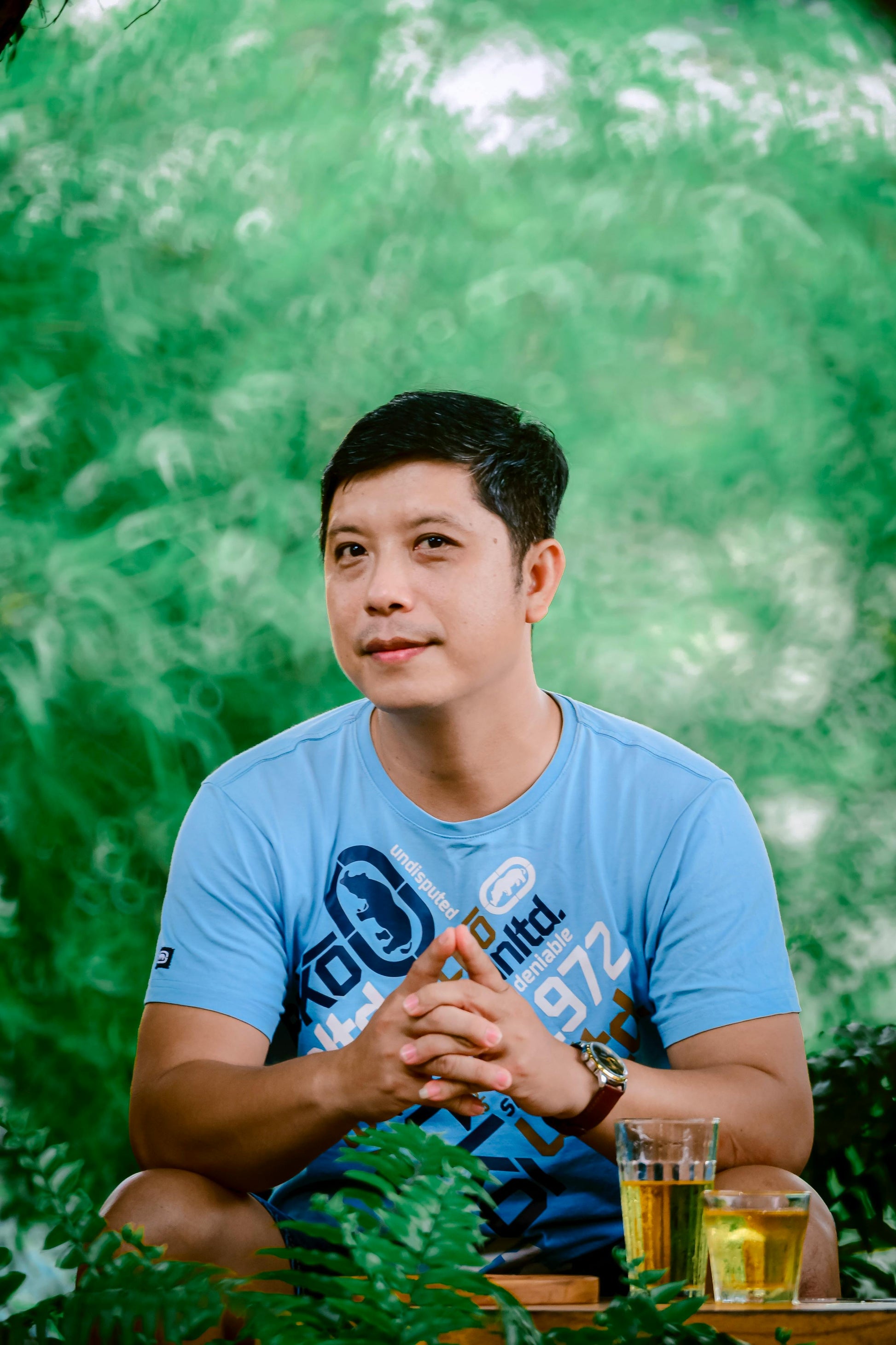 Man wearing blue Ecko Unltd t-shirt with watch, sitting outside with drinks.